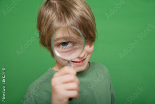 Close up of boy looking through magnifying glass against green background