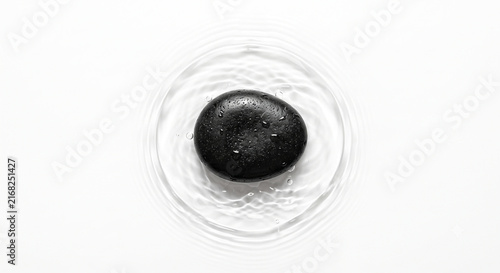 Top-down view of smooth black zen stone with clear water ripples on white background