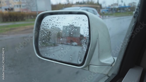 Rainy reflections in a car mirror on a city street