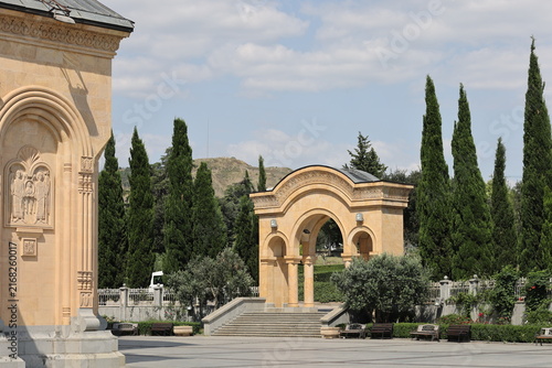 Obraz na plátně Courtyard of Holy Trinity Cathedral (Sameba) in Tbilisi, Georgia with arched pavilion, carved relief and cypress trees under blue sky