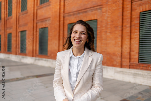 Young businesswoman with a joyful expression standing in front of a modern brick building