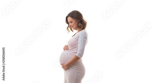Pregnant woman in a light pink dress gently cradling her baby bump with both hands standing against a clean white background side profile.