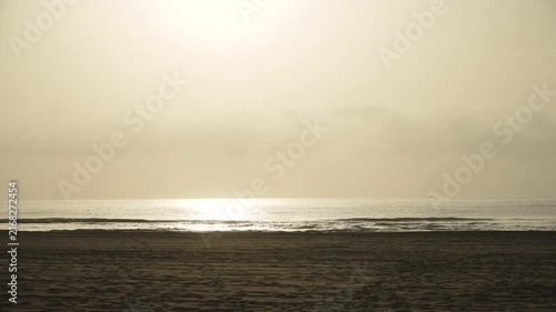 Calm seascape of empty resort coast. Golden soft sunset over sea surf and wide sandy beach at end of velvet holiday season. Birds flying above small sea waves.