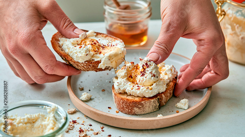 Hands preparing toast with creamy ricotta cheese, honey and chili flakes for a fresh homemade breakfast