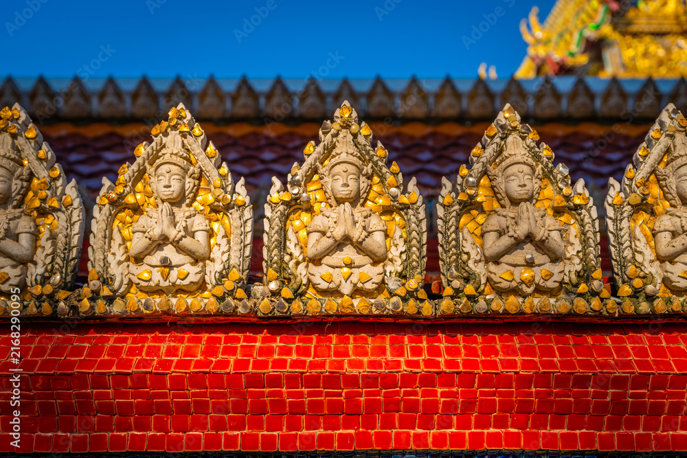 Fototapeta premium Close up of intricate celestial guardian relief sculptures along the red mosaic wall at Wat Sri Uthumphon in Mueang Nakhon Sawan District, Nakhon Sawan, Thailand, showcasing detailed Thai art.
