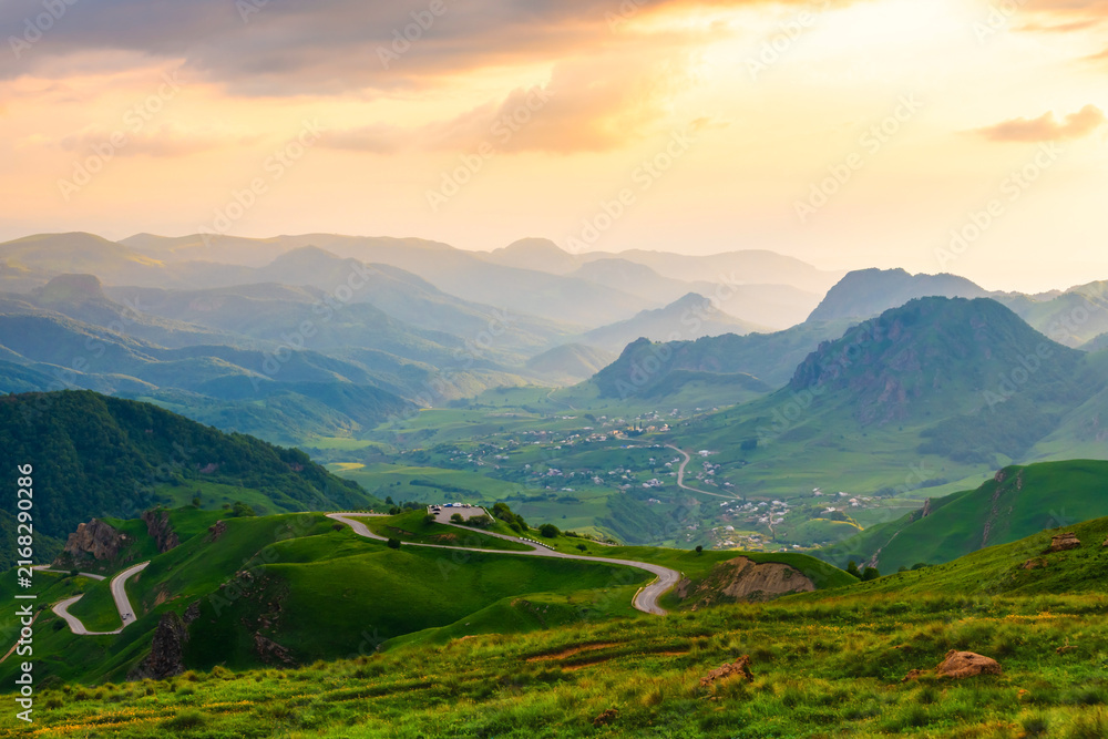 Obraz premium Gumbashi pass in North Caucasus, Russia. View of the green mountains and hills in the evening sunlight. Pink sky with clouds at sunset.