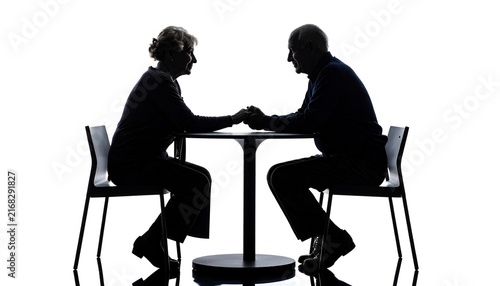 Silhouette of an elderly couple, seated at a small table, holding hands in a sign of intimacy and support. A symbol of enduring love