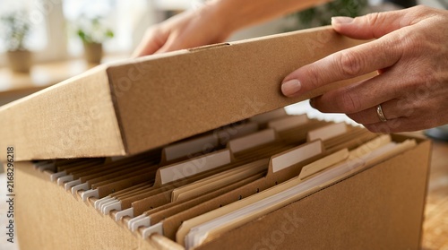 Office worker opening a cardboard storage box filled with organized paper document files.