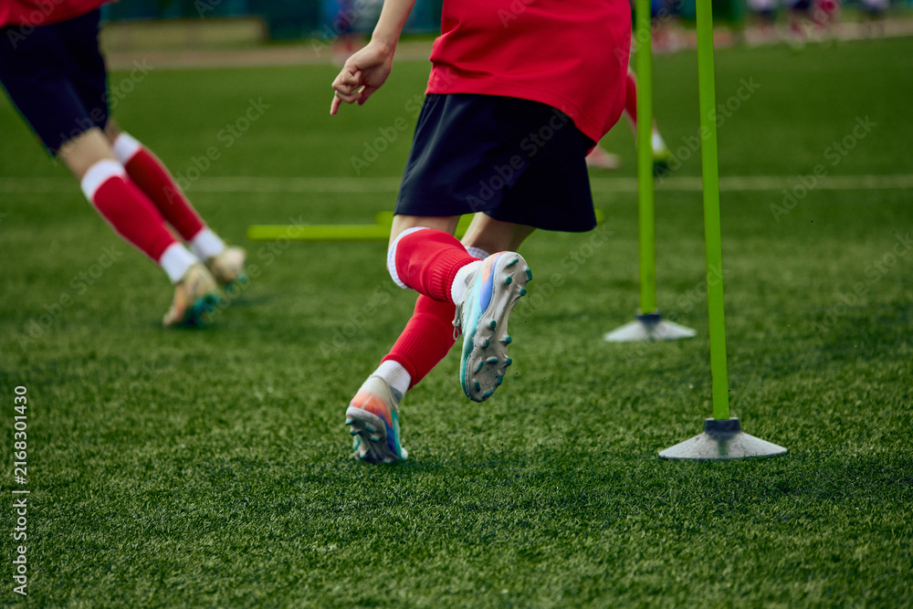 Fototapeta premium Close view of teenage male football player sprinting through agility pole course. Concept of acceleration training, lower body conditioning, sports performance.