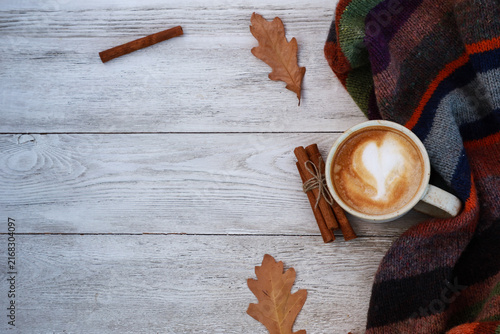 Cup of spicy coffee with milk, dry leaves, warm scarf on white wooden table. Autumn hot drink, fall season concept. Template for seasonal menu. Top view with copy space