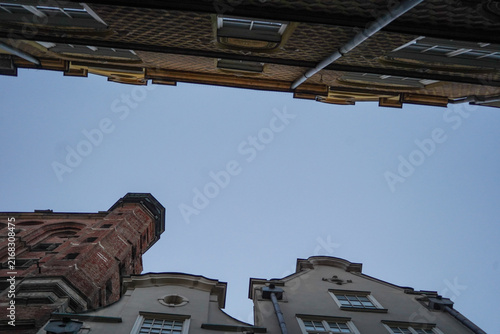 Fotografie Worms-eye perspective shot looking straight up between historic brick buildings and old tenement house eaves framing the clear open blue evening sky above