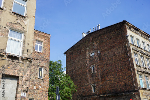 Photography Wide street angle showing historic weathered brick tenement buildings and decaying facades in Gdansk, Poland, under a clear blue sky