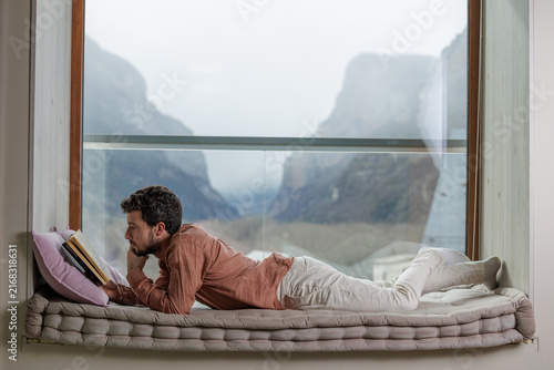 Young man reading a book by a window in a peaceful moment of learning and relaxation