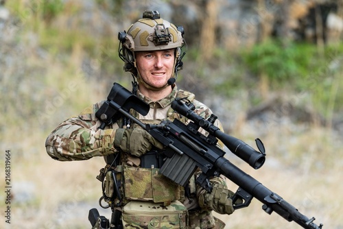 Картината върху платно Soldier stands outdoors holding a rifle while wearing tactical gear in a trainin