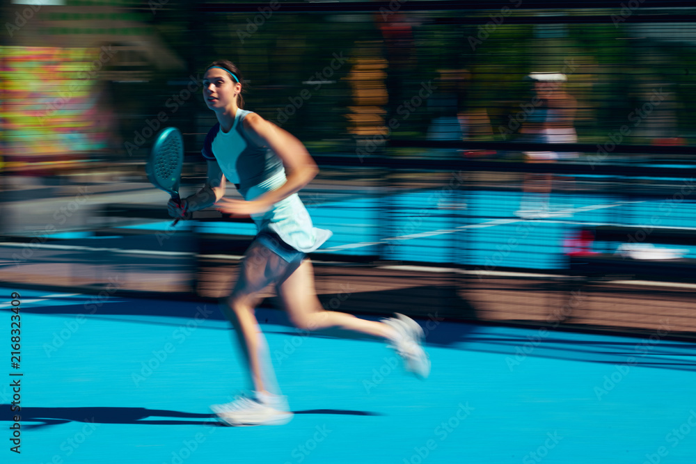 Fototapeta premium Female padel athlete in stylish blue sportswear running with cinematic motion blur on court. Concept of motion fashion campaign, energetic activewear, youth sport style.