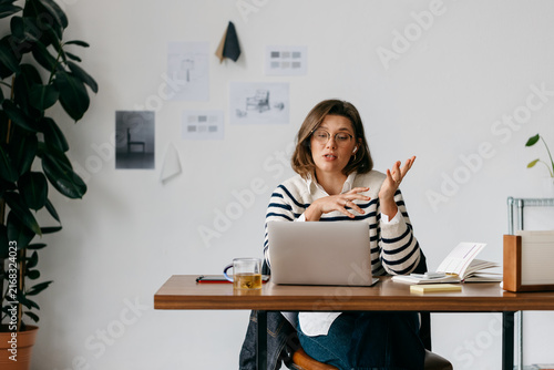 The woman speaks in a creative workspace while working on her laptop