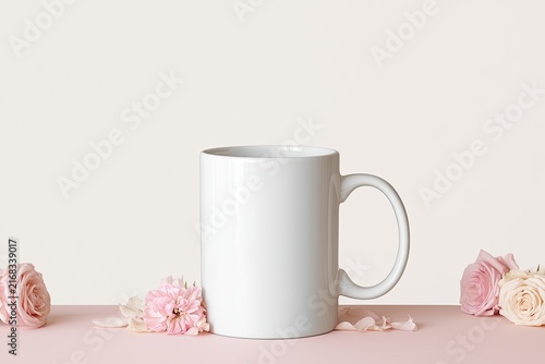 A clean white mug sits on a pink surface, adorned with delicate pink and cream roses