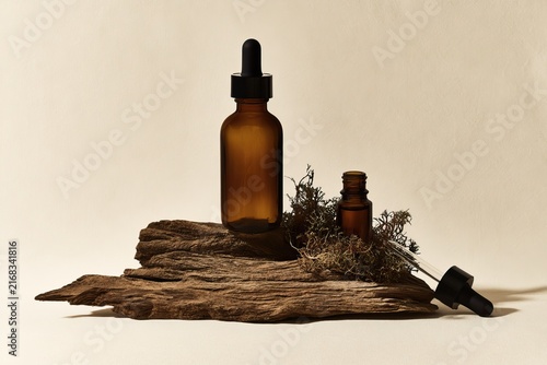 Two amber glass dropper bottles with dark stoppers on driftwood with moss