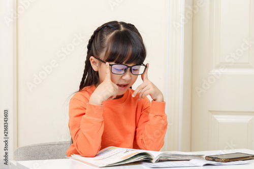 Obraz na płótnie Studious girl adjusting her glasses while concentrating deeply on an open textbook