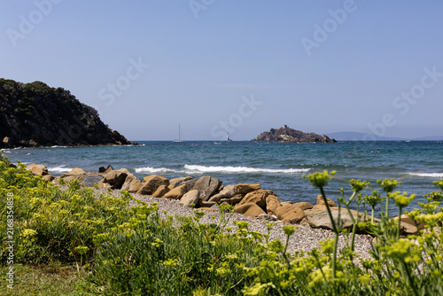 Scenic beach at Punta Ala, Tuscany, Italy, with the blue Mediterranean Sea and a distant island on the horizon. Peaceful Tuscan coastal landscape surrounded by Mediterranean vegetation.