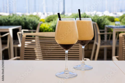Italian caffè shakerato served in a wine glass, photographed with the marina of Punta Ala in Tuscany. Refreshing iced coffee drink with a scenic Mediterranean harbor view.