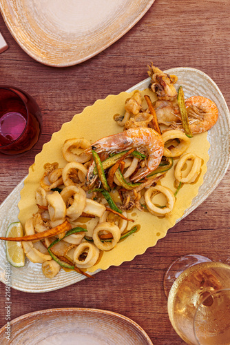 Italian mixed fried seafood served on an oval plate, featuring crispy fried calamari rings, small cuttlefish, shrimp and fried vegetables. Mediterranean cuisine. Vertical image.