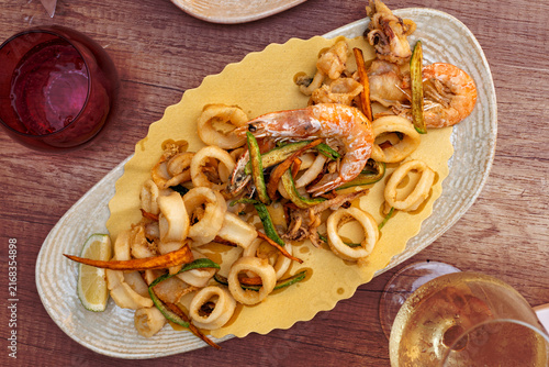 Italian mixed fried seafood served on an oval plate, featuring crispy fried calamari rings, small cuttlefish, shrimp and fried vegetables. Mediterranean cuisine.