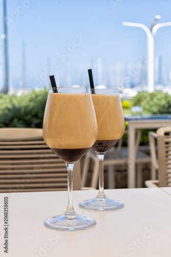 Italian caffè shakerato served in a wine glass, photographed with the marina of Punta Ala in Tuscany. Refreshing iced coffee drink with a scenic Mediterranean harbor view. 