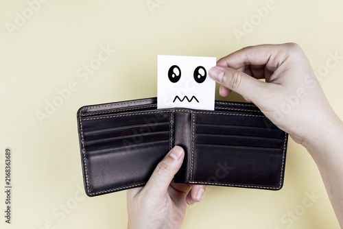 Hands opening empty leather wallet with worried sad face card. Concept of empty wallet, no money, financial crisis, debt, and economic problem.