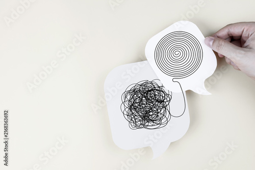 Hand holding speech bubble paper cut with messy tangle line untangled into organized spiral. Concept of mental health, therapy, problem solving, and clarifying thoughts.