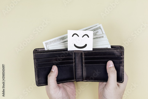 Hands opening leather wallet full of cash with happy smile face card. Concept of financial freedom, wealth happiness, and money savings success.
