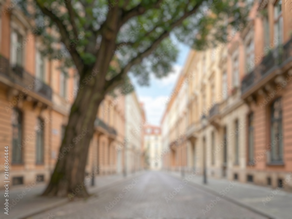 Fototapeta premium Blurred urban street lined with historic architecture, trees, balconies, and residential buildings, representing travel, city life, culture, and heritage.