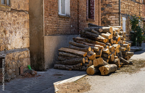 View of a large pile of stacked firewood logs resting against a rustic brick and stone wall in the historic village of Vevchani, Vevcani Municipality, North Macedonia.
