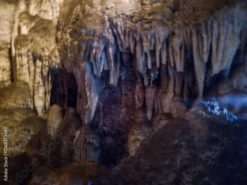 Massive limestone stalactites hanging from the dark rugged ceiling inside a deep subterranean cavern create a textured natural display captured with soft ambient interior lighting