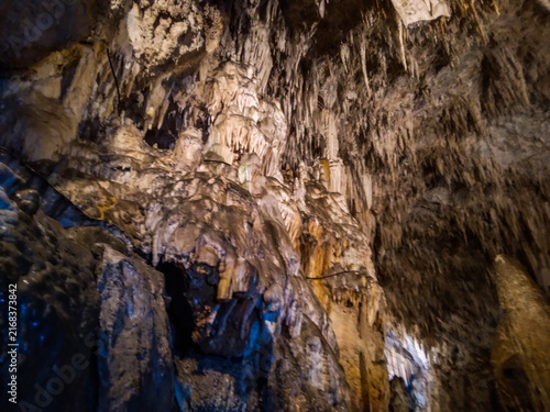 Foto Limestone stalactites and stalagmites hanging from the dark rugged cavern ceilin