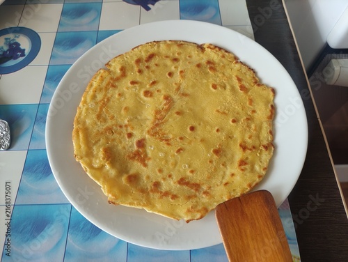 Large golden fried flatbread pancake served on a white plate with wooden spatula