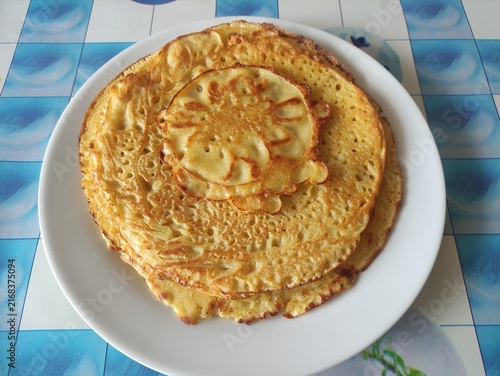 Stack of golden fried pancakes with a smaller pancake on top served on a white plate
