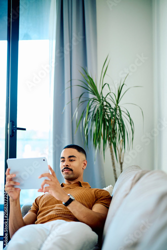 Fotografía Young man relaxing on a comfortable sofa at home, engrossed in content on a digital tablet