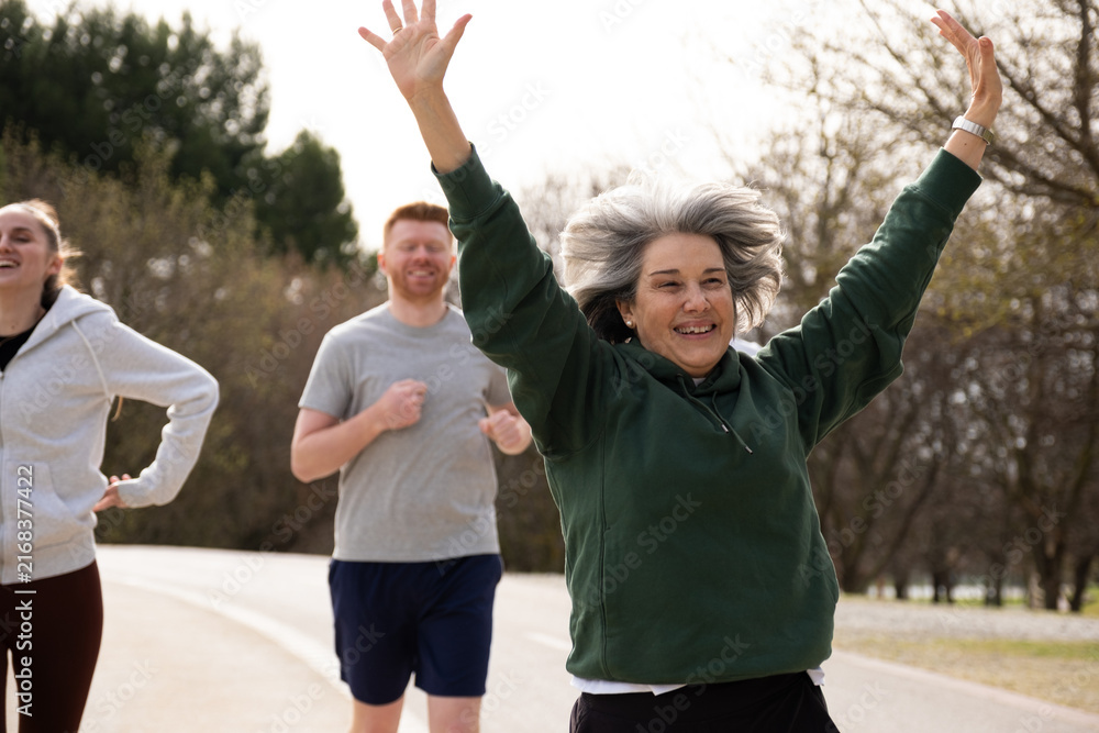 Obraz premium Smiling older woman celebrating success during a run with a diverse group