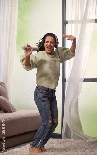 A STYLISH YOUNG WOMAN HAPPILY DANCING WHILE LISTENING TO MUSIC AT HOME