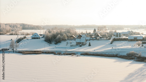 Aerial winter panorama of a frozen river winding through snowy fields with a small village on the bank, lithuania winter tourism content, christmas card background, rural travel marketing
