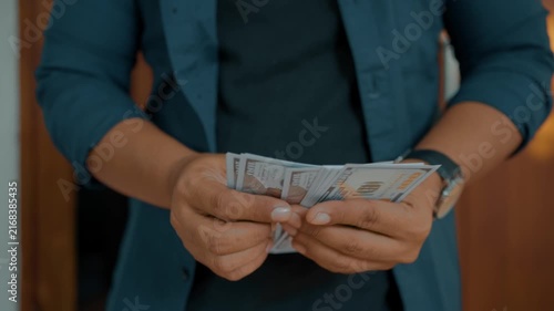 Man investor counting US Dollar bills, close-up. Male trader holds bundle of money, Considers USD at home. Person manages budget.