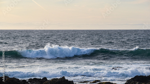 Принти на полотні Wide coastal seascape featuring a powerful breaking ocean wave, textured blue water and soft open sky with ample copy space