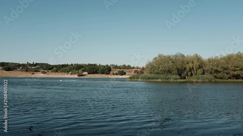 Calm river under a clear blue sky, with lush green trees and reeds along the riverbank. For environmental conservation campaigns, travel promotional videos, or peaceful background visuals.