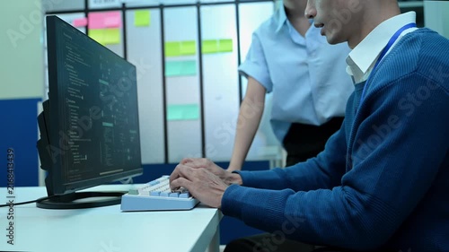 Two Asian software developers collaborating, discussing source code on screen, and troubleshooting