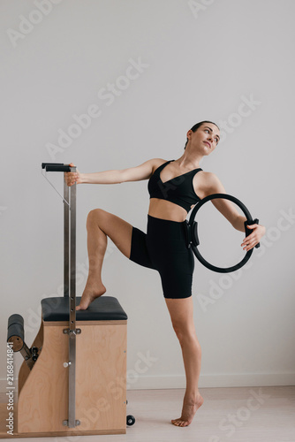 Woman holds a pilates ring while balancing on a reformer chair