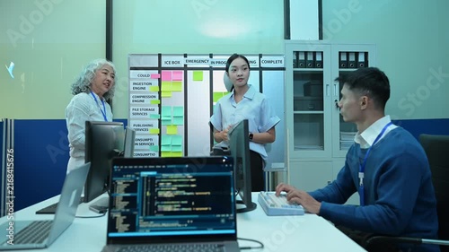 Diverse IT software engineering team discussing project workflow and agile sprint planning on sticky note board