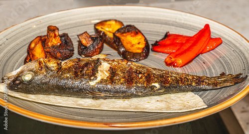 Delicious grilled sea bass and sea bream fish served on a plate with fresh lemon slices, rosemary, and olive oil. Healthy Mediterranean dinner concept.