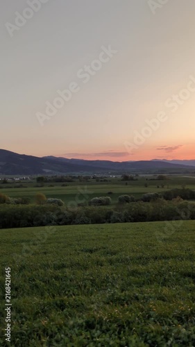 Scenic golden sunset over mountain ridge and green meadow landscape, peaceful evening horizon with orange sky during twilight countryside road trip journey in summer nature background view