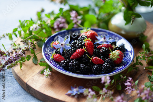 Alpine starwberry  - Fragaria vesca and blackberry fruit on a vintage English plate with fresh herbs -  soft fruit garden treat.
